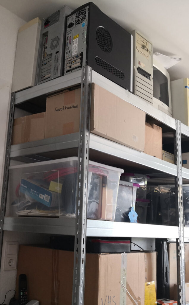 Shelf with lots of moving boxes, plastic boxes, computers, and other stuff. Upper left part.